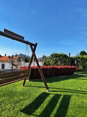 Ein Holzschaukelgerüst in einem gepflegten Rasenbereich mit einer Hecke und blauem Himmel.