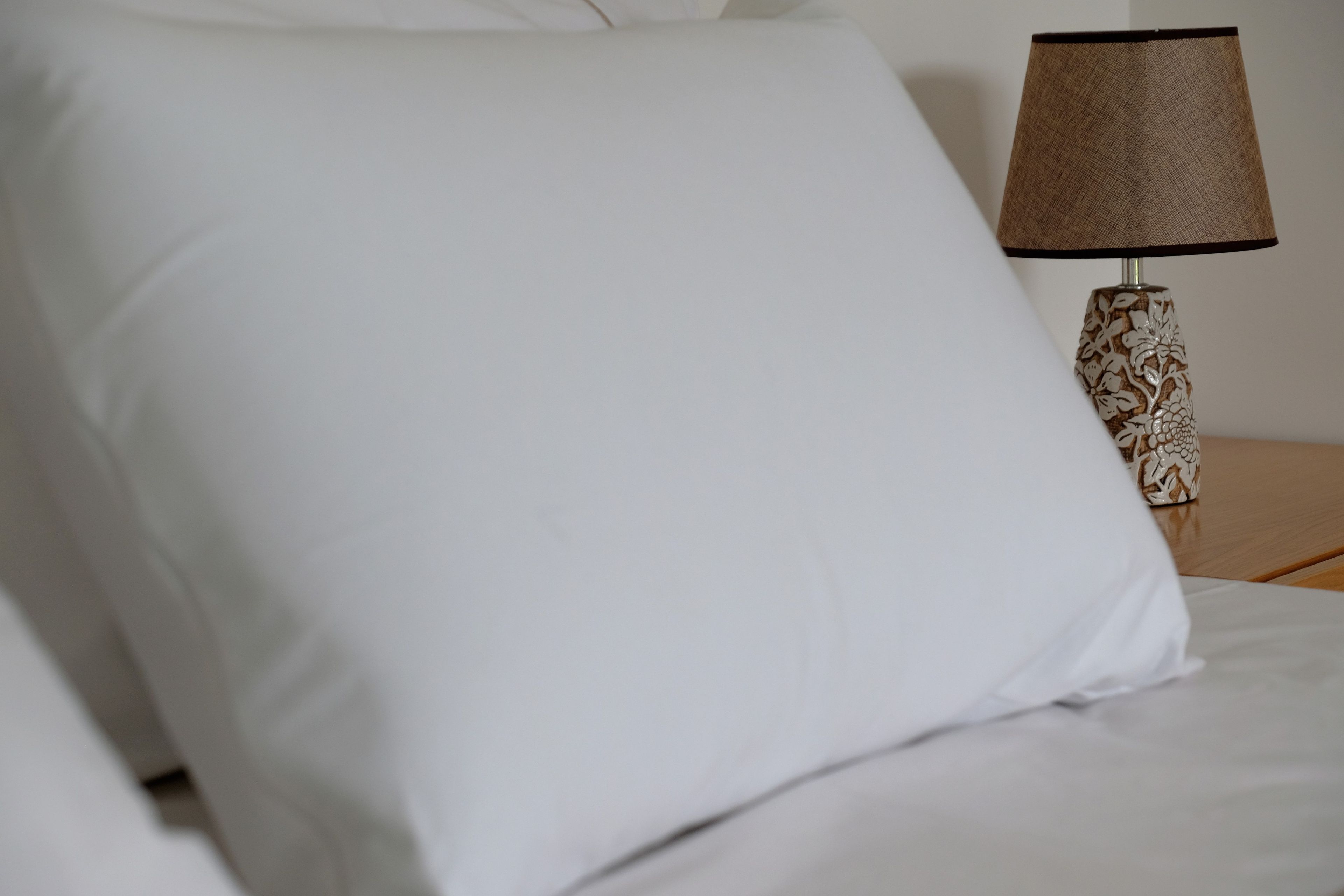 Un llit ben arropat amb llençols blancs i una làmpada decorativa amb pantalla de fibra sobre una tauleta de nit de fusta.
