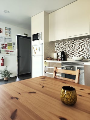 A modern kitchen with white cabinets, a microwave, and a refrigerator. There is a wooden dining table with a bowl and a mug. - Tiny Home 'Casa Amarela' with Sea View, Shared Pool and Wi-Fi (Cristelo)