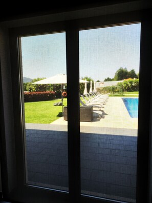 Blick durch ein Fenster auf einen Poolbereich mit Liegestühlen und Sonnenschirmen.