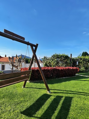 Un columpio de madera en un área verde cuidada, con seto y cielo despejado.