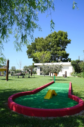 Un parque infantil con tobogán y zona de escalada, rodeado de césped y árboles.