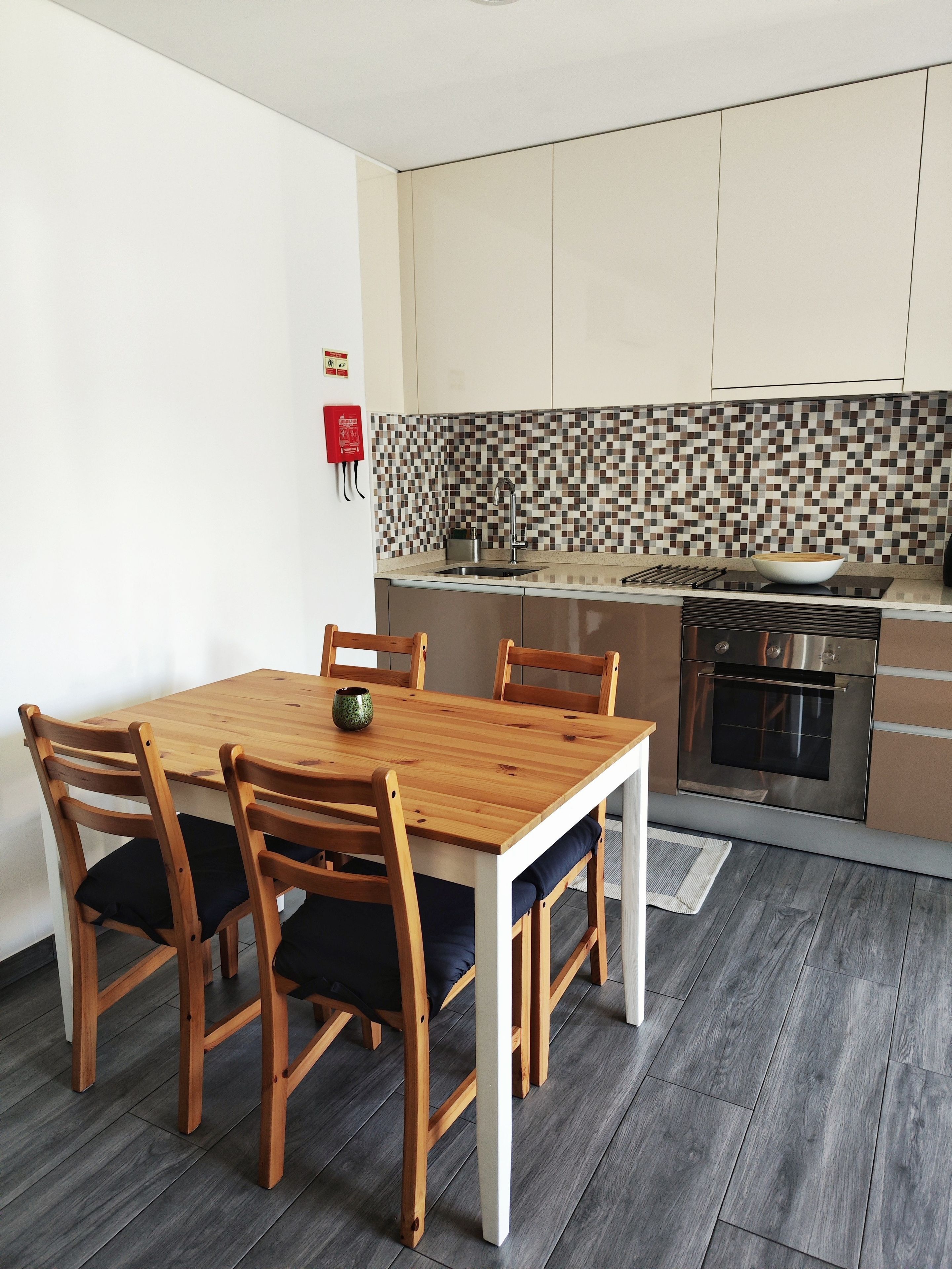 A modern kitchen with a tiled backsplash, a built-in oven, and a dining area with a wooden table and chairs.