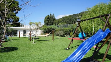 A playground with a blue slide and swings, surrounded by a grassy area and trees.
