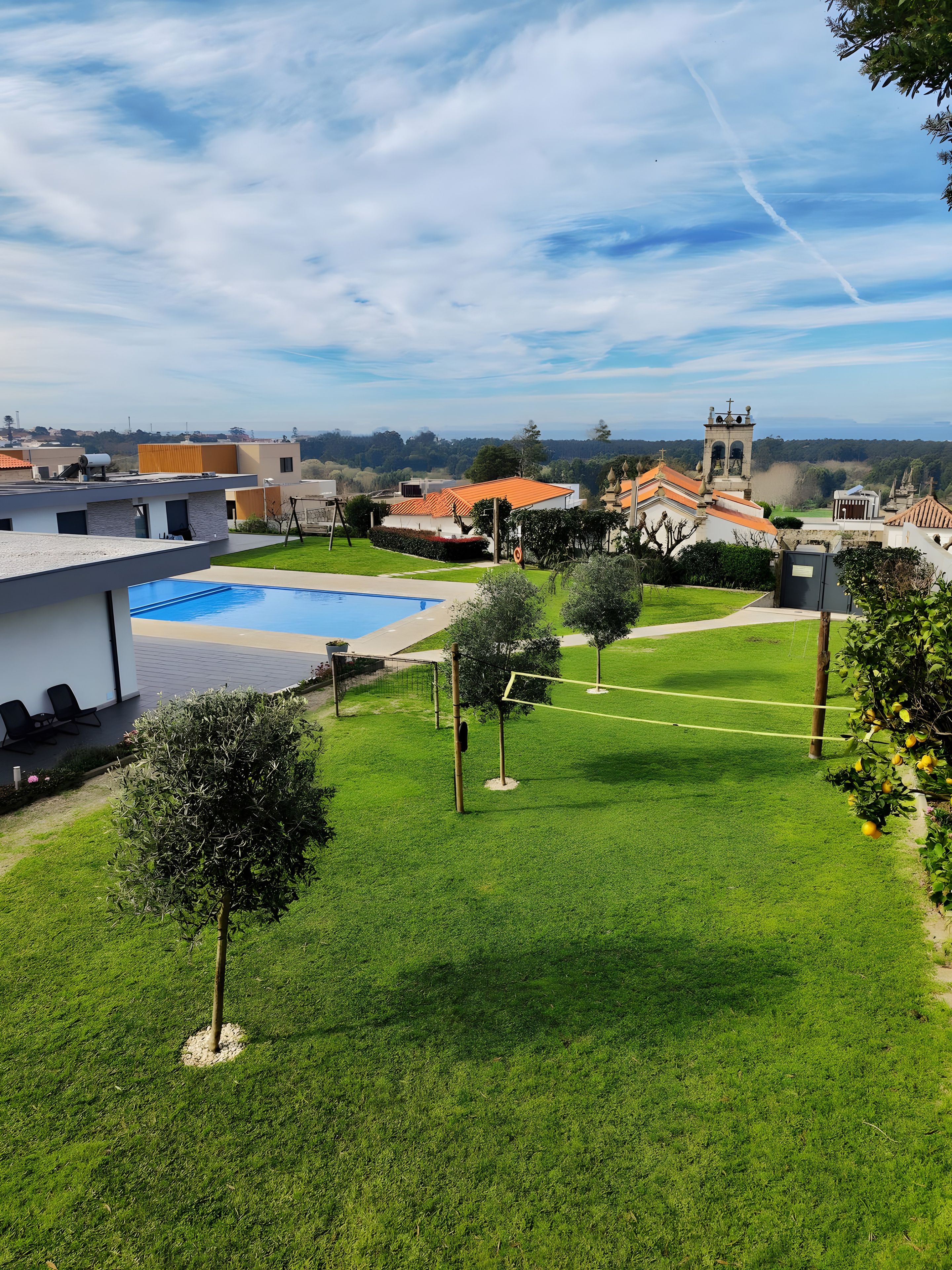 A residential area with a swimming pool, a tennis court, and a church in the background.