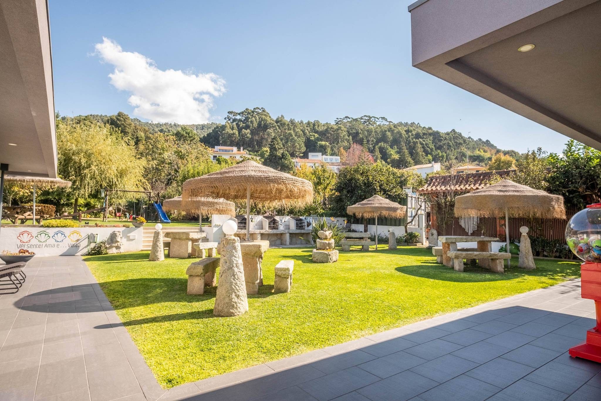An outdoor area with stone benches, thatched umbrellas, and a grassy lawn.