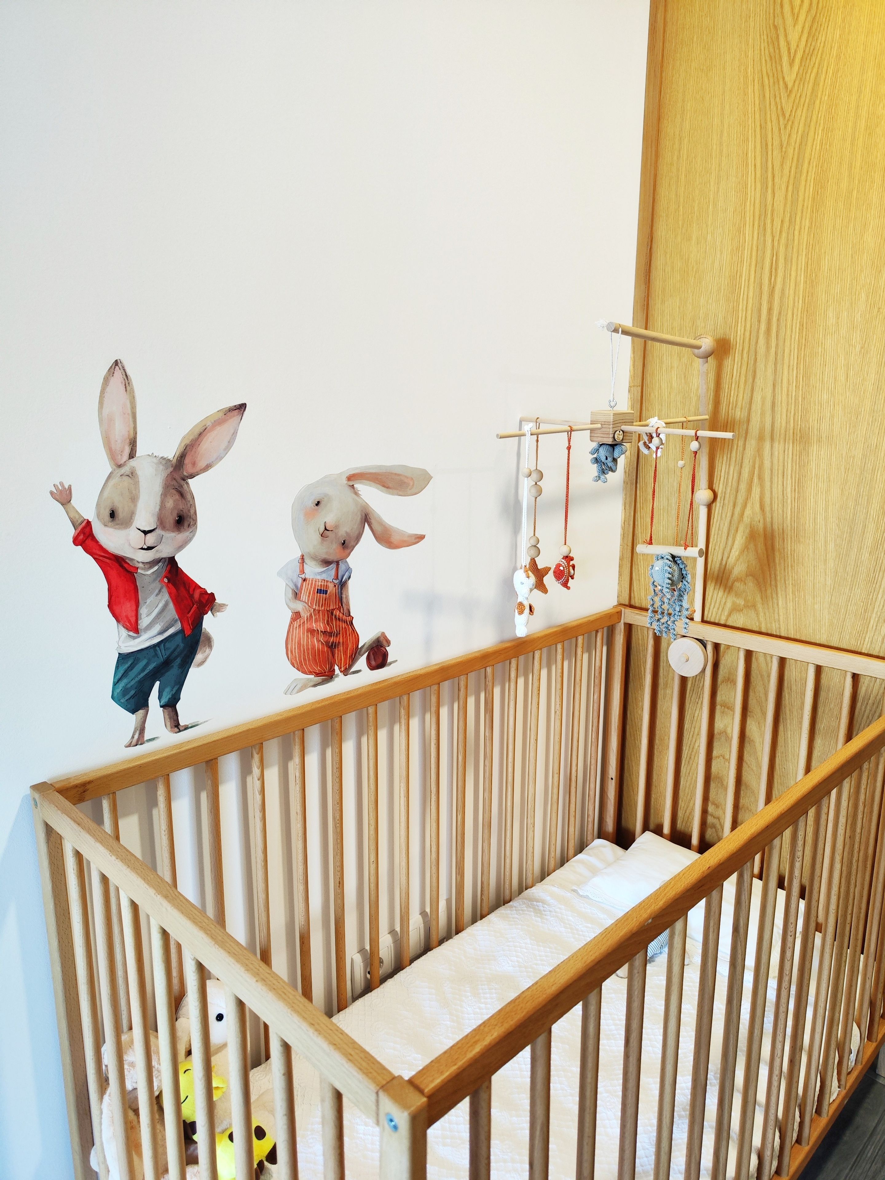 A wooden crib with a mattress and a wall-mounted mobile with hanging toys.