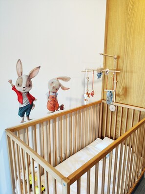 A wooden crib with a mattress and a wall-mounted mobile with hanging toys. - Tiny Home 'Casa Amarela' with Sea View, Shared Pool and Wi-Fi (Cristelo)