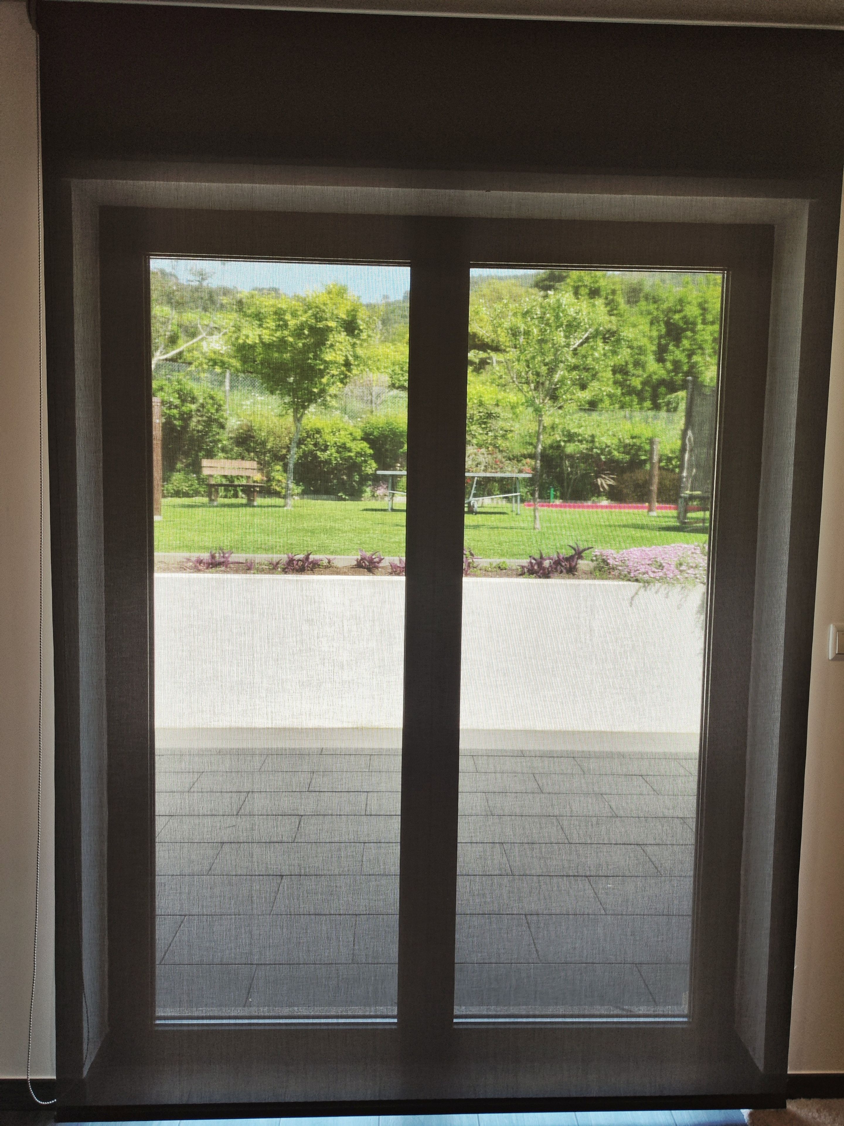 Blick durch eine Tür mit Fenster auf eine gepflasterte Fläche mit Bank und Grünpflanzen.