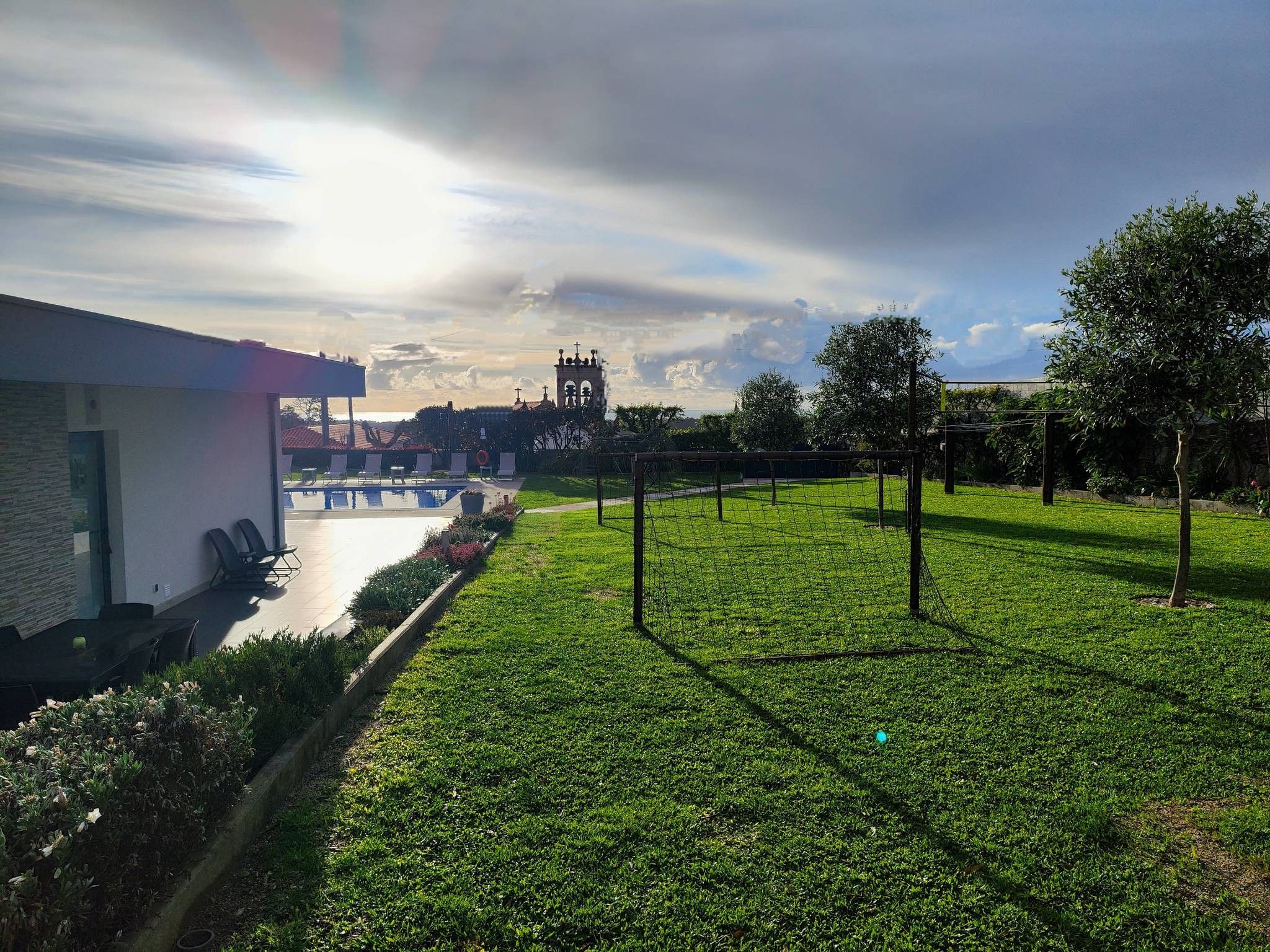 A grassy area with a pool, lounge chairs, and a building with a red roof.