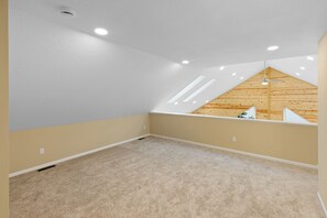 Ein Zimmer mit schrägem Dach, eingebetteter Beleuchtung und sichtbarem Dachboden mit Holzbalken.