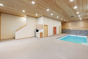 Amplio espacio interior con piscina, techo de madera y pared de piedra.