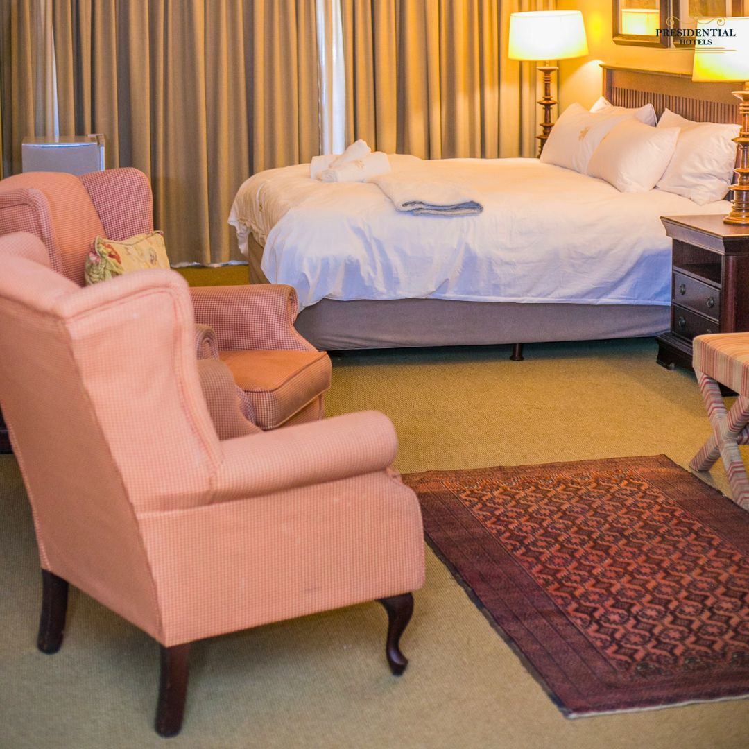 Habitación de hotel con una cama, una silla, una mesita de noche, una lámpara y una alfombra estampada.