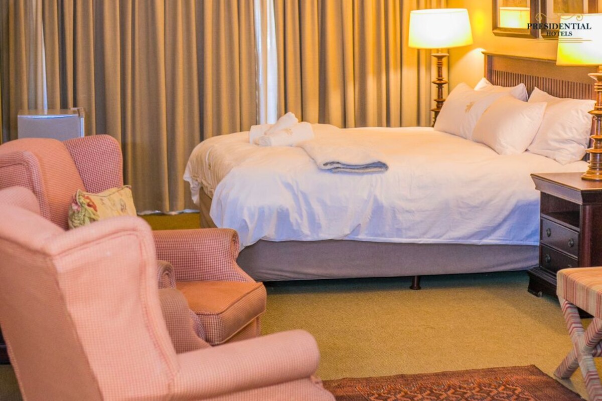 Ein Hotelzimmer mit Bett, Sessel, Nachttisch, Lampe und einem gemusterten Teppich.
