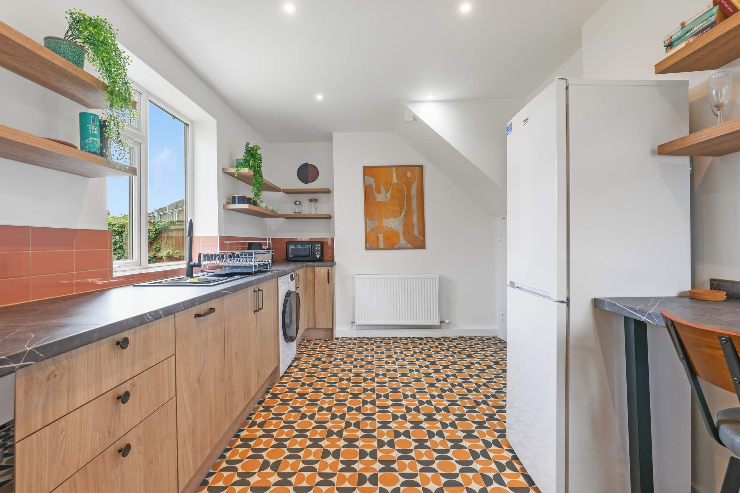 Une cuisine moderne avec un carrelage à motifs, des meubles en bois et un lave-linge encastré.