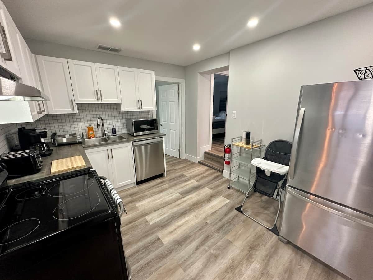 A modern kitchen with white cabinets, stainless steel appliances, and a wooden floor.