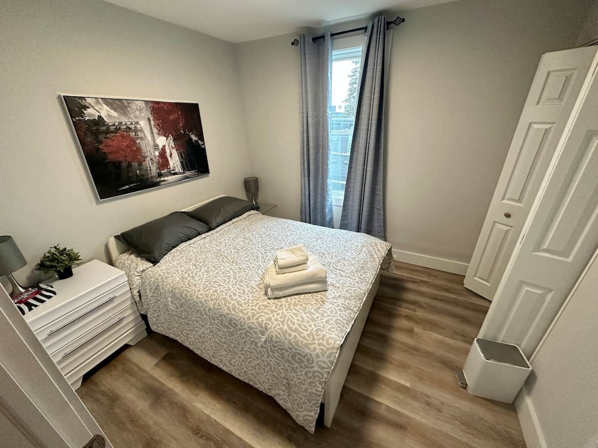 A bedroom with a bed, bedside tables, a nightstand, a window with curtains, and a door.