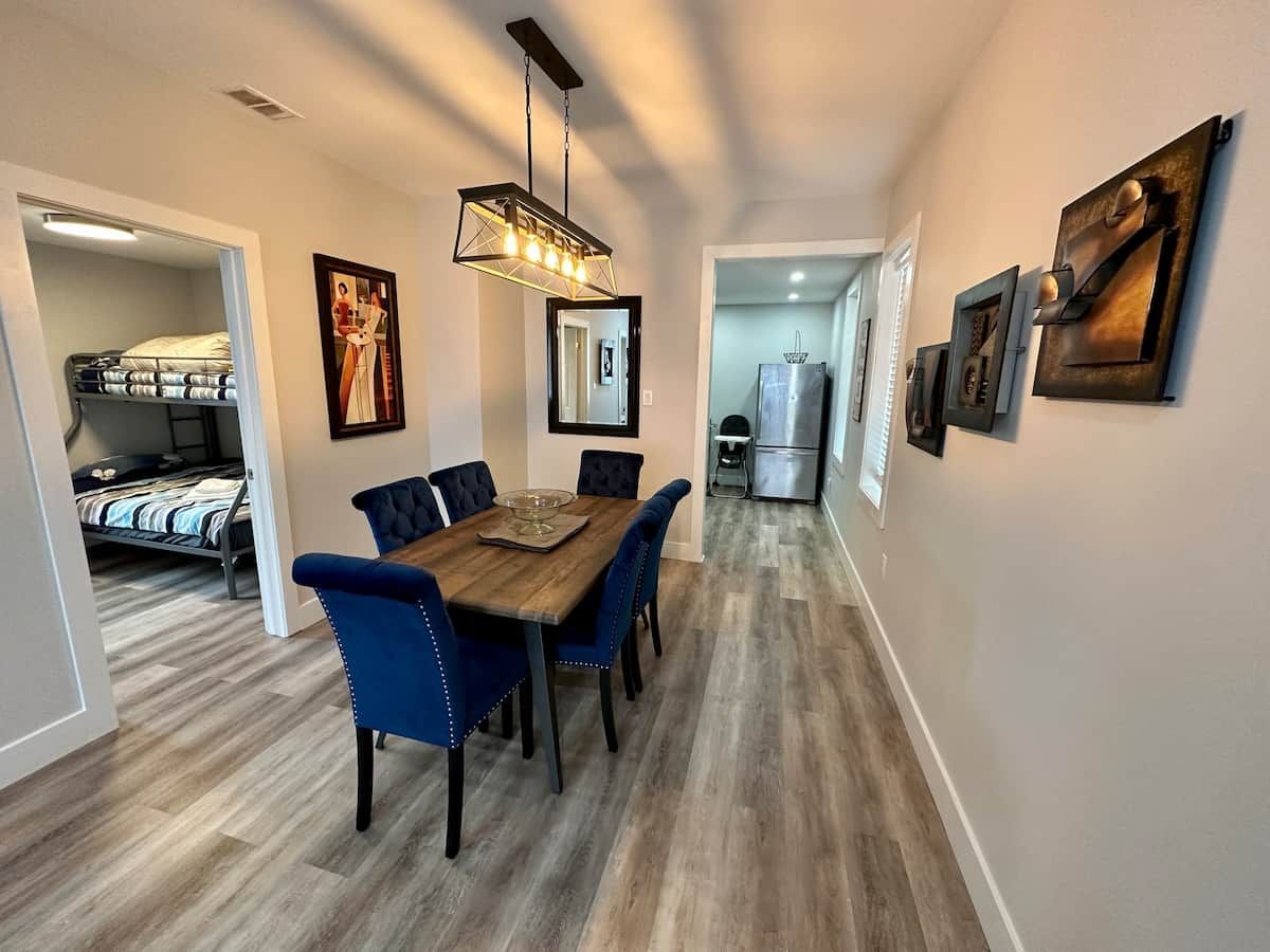A dining area with a wooden table and blue upholstered chairs, a hanging light fixture, and artwork on the walls.