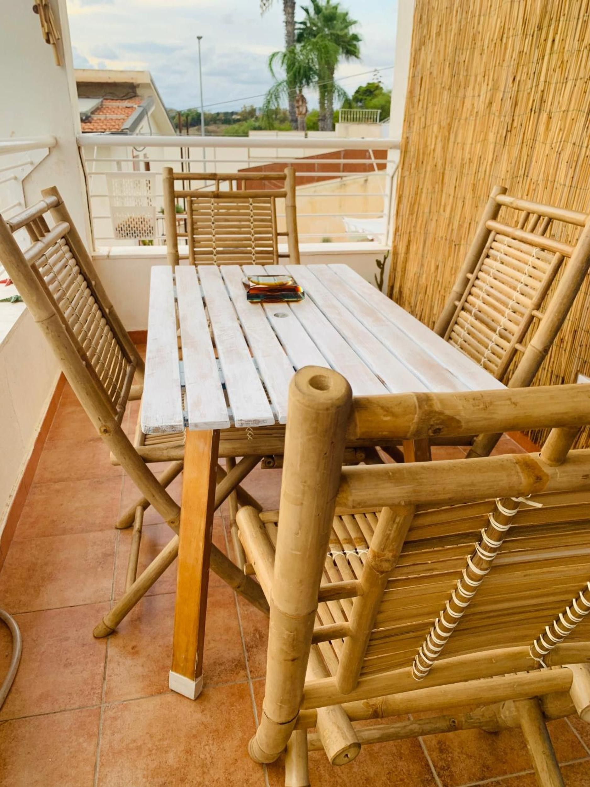 A wooden table and chairs set on a balcony with a view of palm trees and a building in the background.
