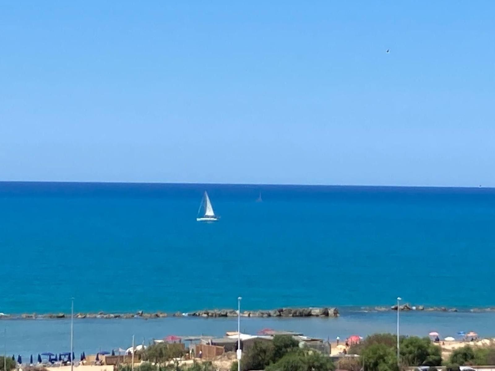 Une vue sur la côte, avec un voilier sur l’eau, une côte rocheuse et des parasols de plage.
