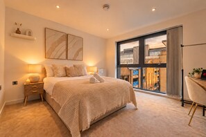Een moderne slaapkamer met een groot bed, nachtlampjes, uitzicht door een schuifdeur en een laptop op een bureau.