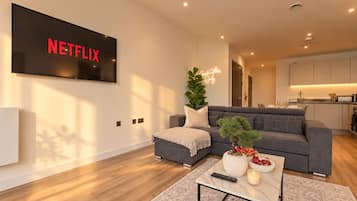 A modern living room with a grey sofa, a coffee table with a remote control, a lit candle, and a potted plant.