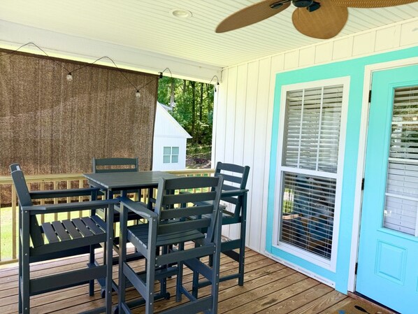 A covered outdoor area with a table and chairs, a ceiling fan, and a view of a house through a window.