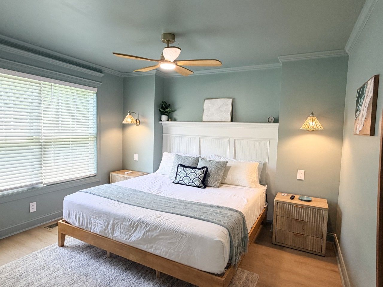 Une chambre à coucher avec un lit, des tables de chevet, un ventilateur de plafond et une fenêtre avec des stores.