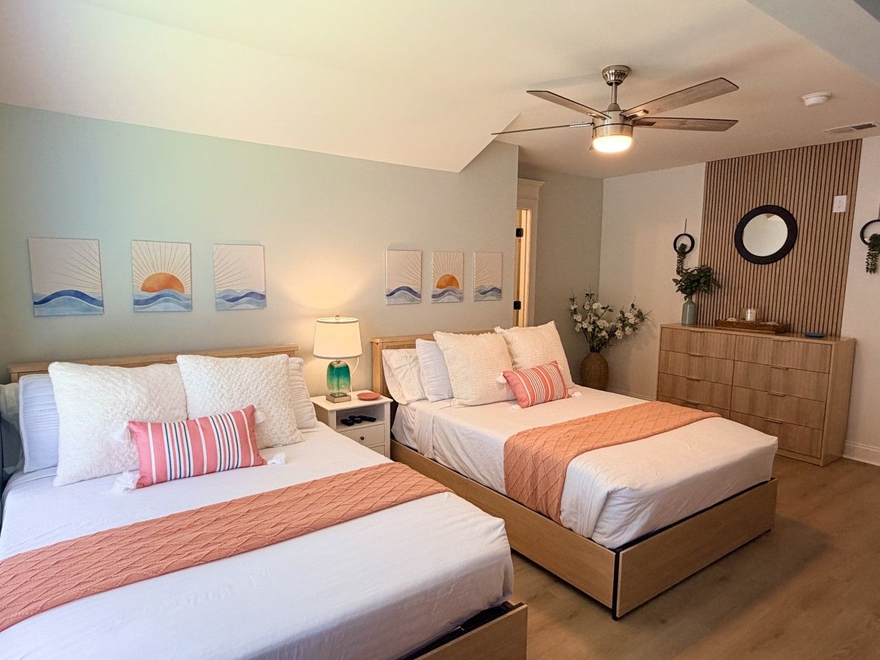 Une chambre d’hôtel avec deux lits, un ventilateur de plafond, des œuvres d’art accrochées aux murs et une armoire en bois.