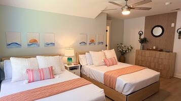 Une chambre d’hôtel avec deux lits, un ventilateur de plafond, des œuvres d’art accrochées aux murs et une armoire en bois.