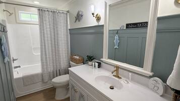 A bathroom with a bathtub, toilet, vanity with a sink, and a large mirror.