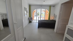 Een slaapkamer met een bed, een stoel, een raam met gordijnen en een deur.