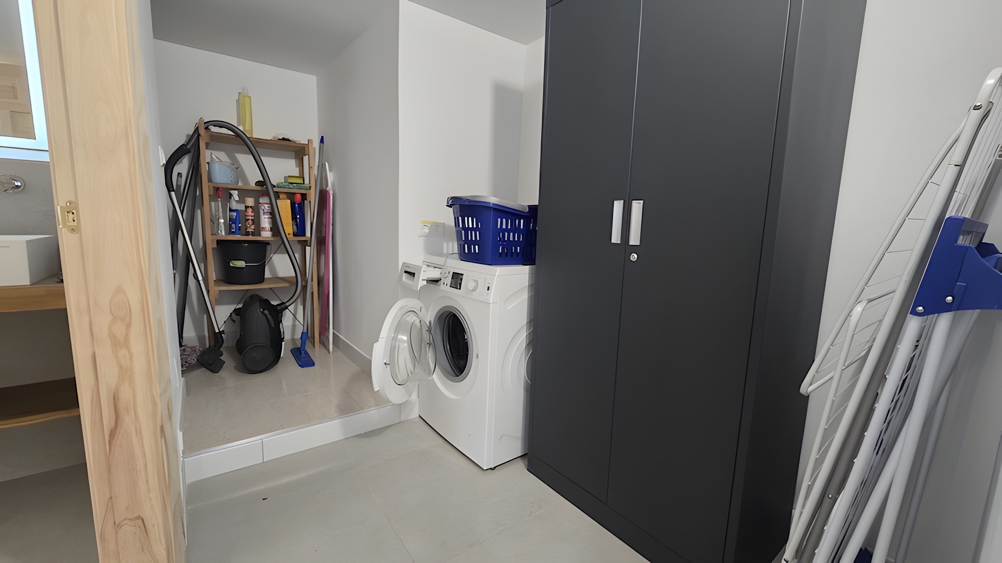 Une buanderie équipée d’un lave-linge, d’un sèche-linge et d’une étagère contenant des produits de nettoyage.