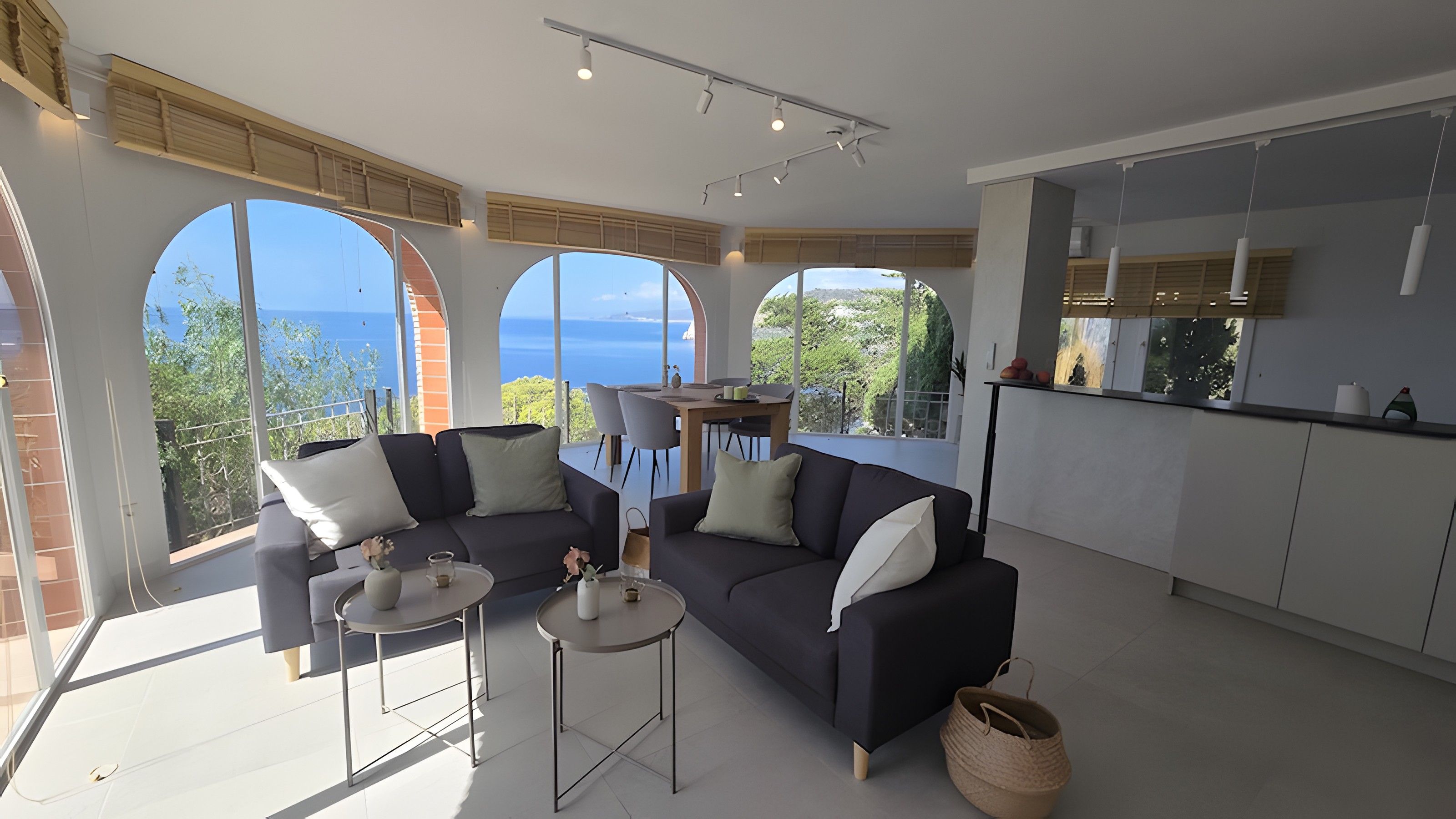 Un espace de vie moderne comprenant un canapé, une table basse et un coin repas, avec de grandes fenêtres offrant une vue sur la mer.