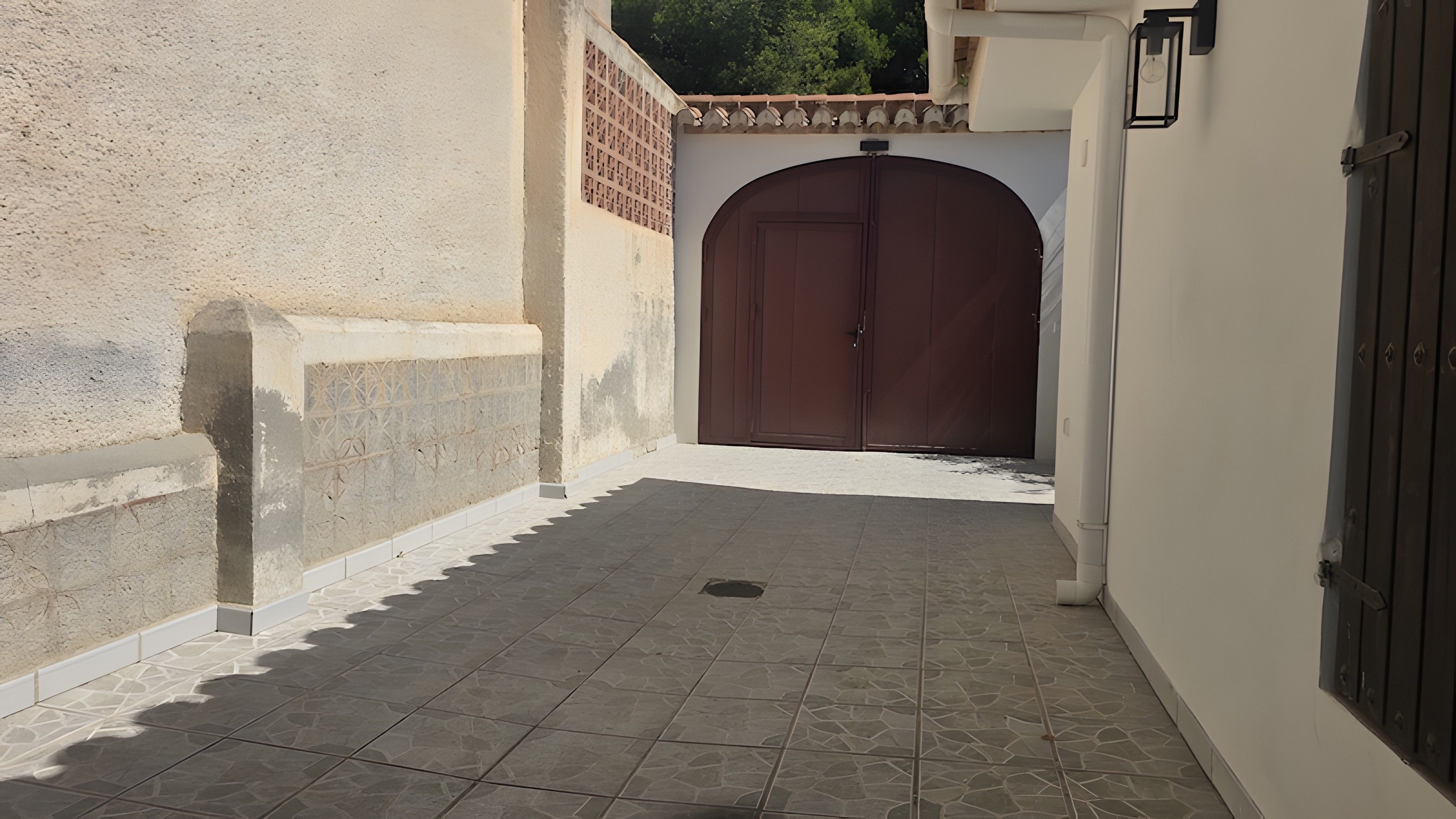 Un callejón estrecho con piso de baldosas que conduce a una puerta de madera grande.