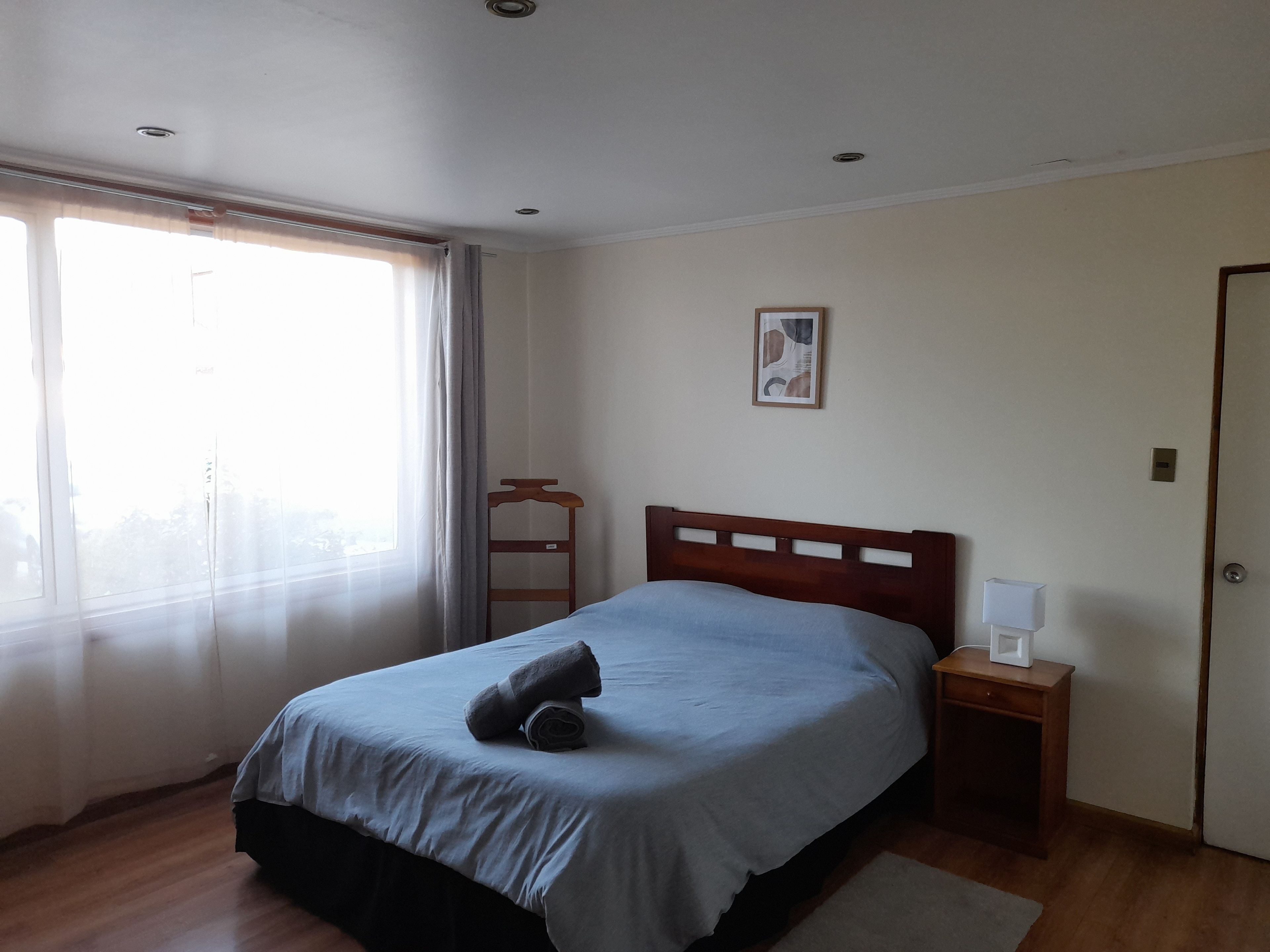 Une chambre à coucher avec un lit, une table de chevet, une lampe, une fenêtre avec des rideaux et une porte.