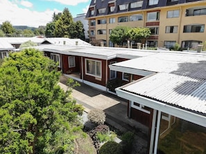 A residential building with a flat roof, multiple windows, and a garden area with trees.