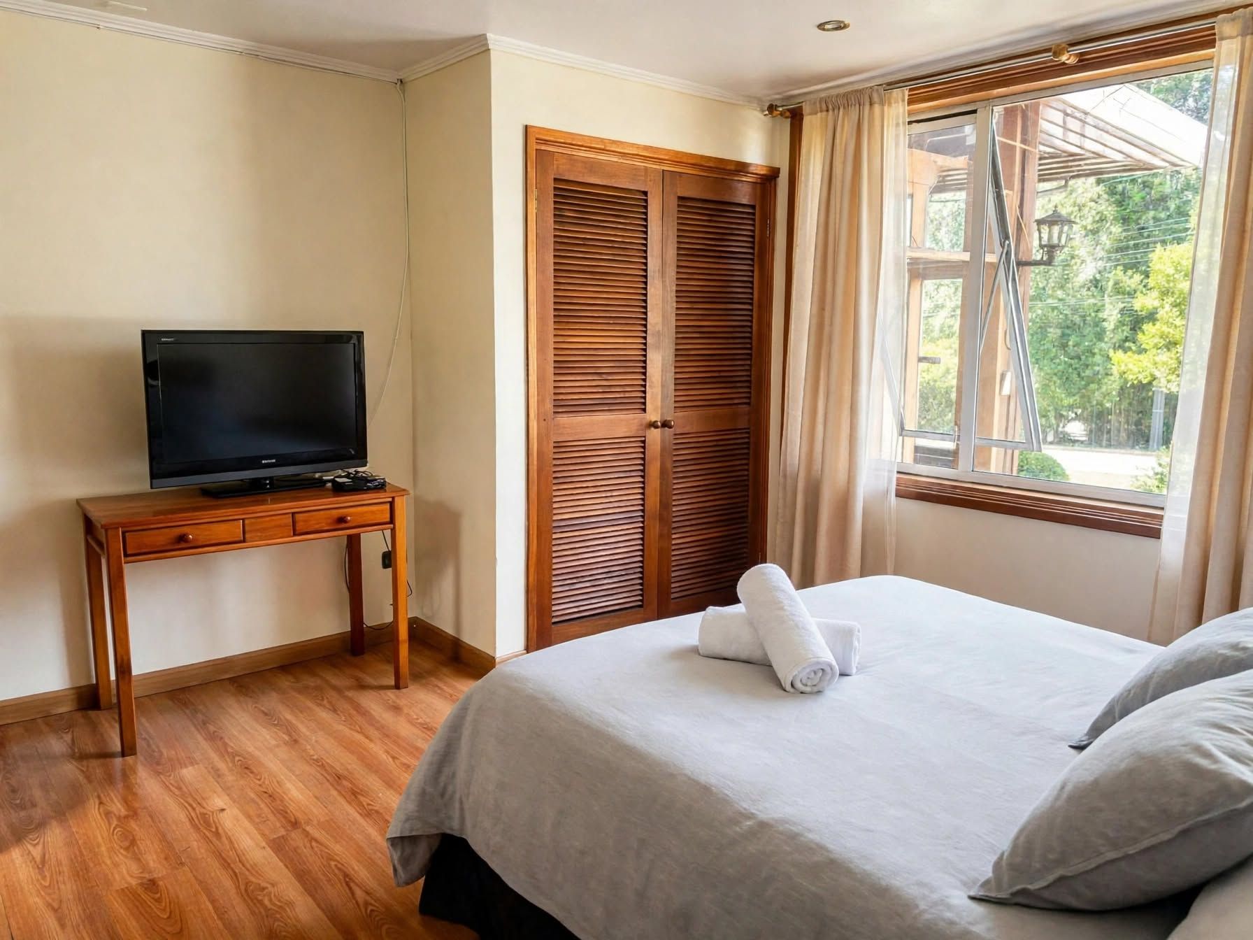 Une chambre d’hôtel avec un lit, un téléviseur posé sur une table en bois et une fenêtre avec des rideaux.