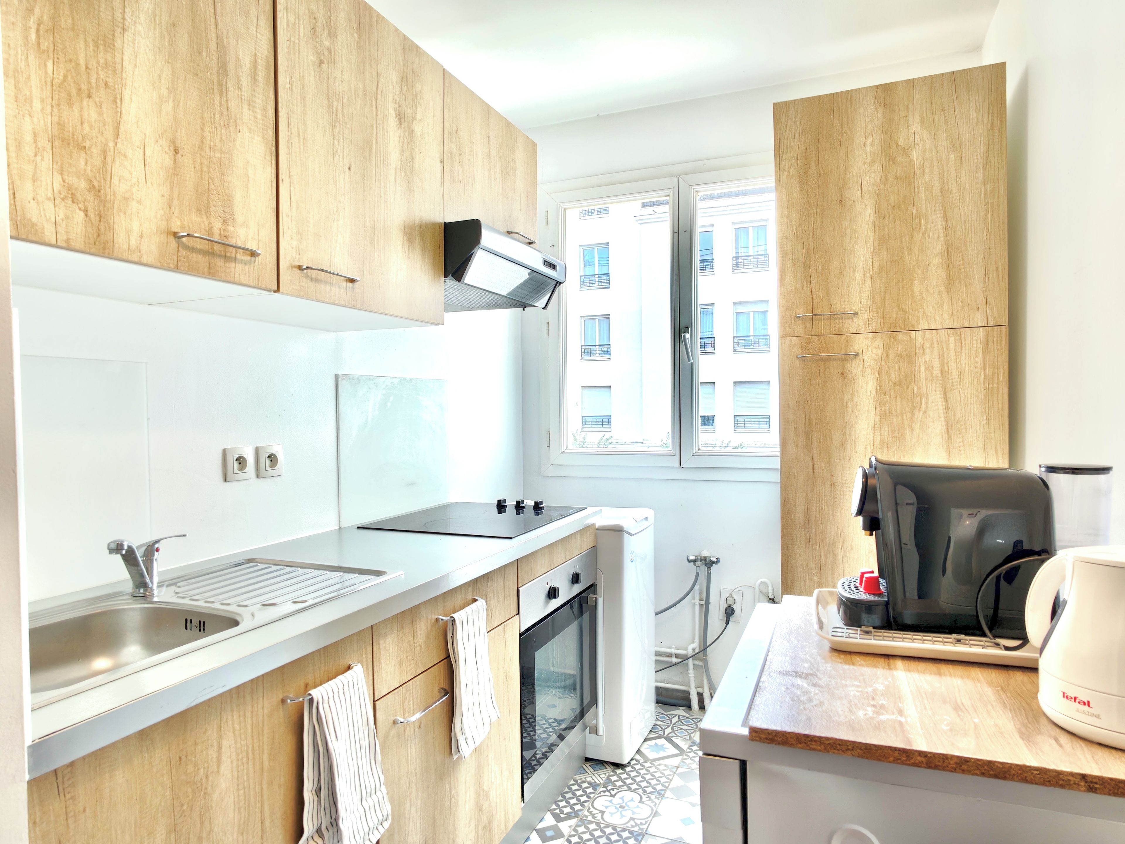 Een moderne keuken met houten kastjes, een roestvrijstalen spoelbak, een inbouwoven en een koffiezetapparaat.