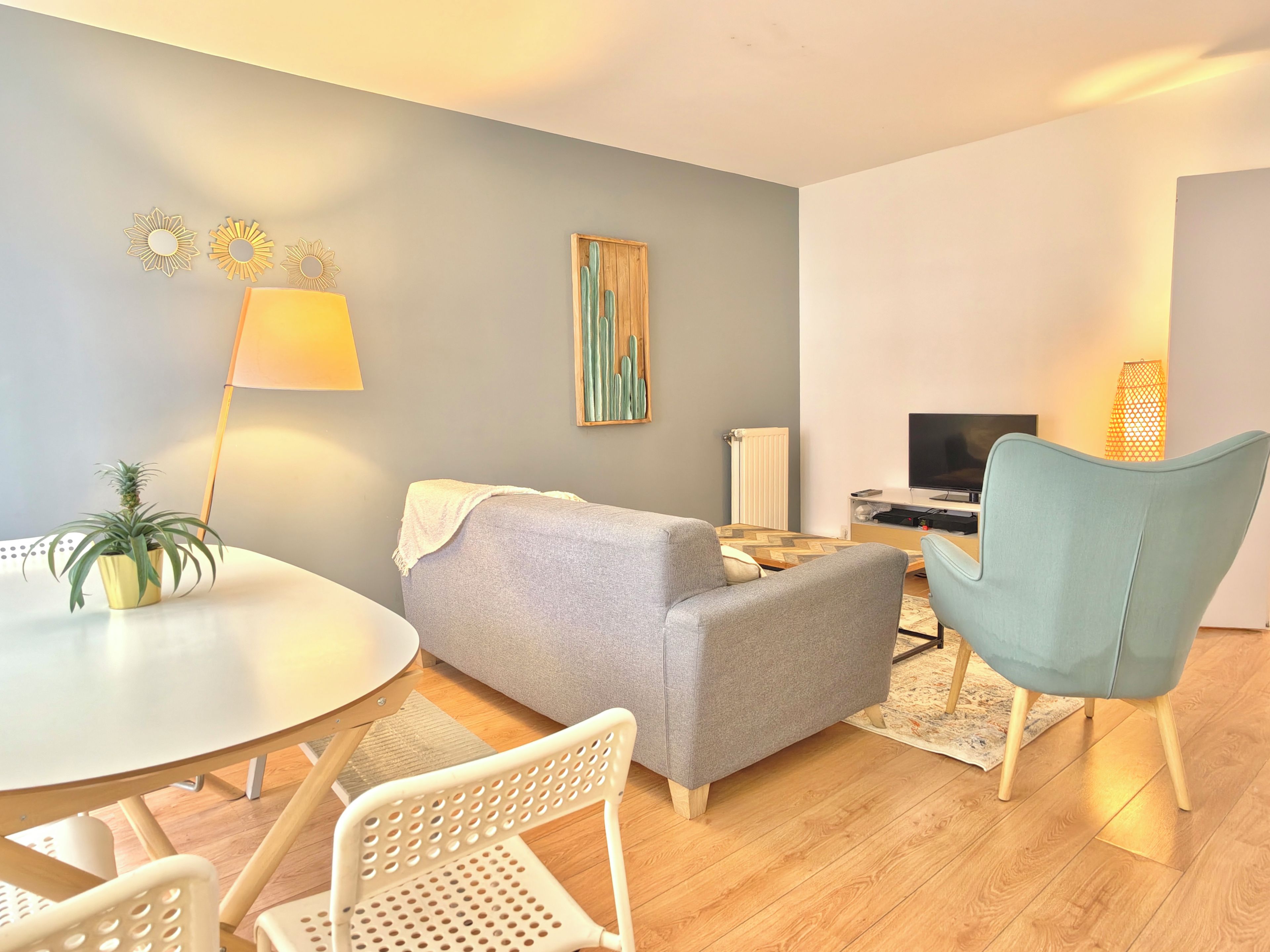 A modern living room with a grey sofa, a round table, a potted plant, and a television.