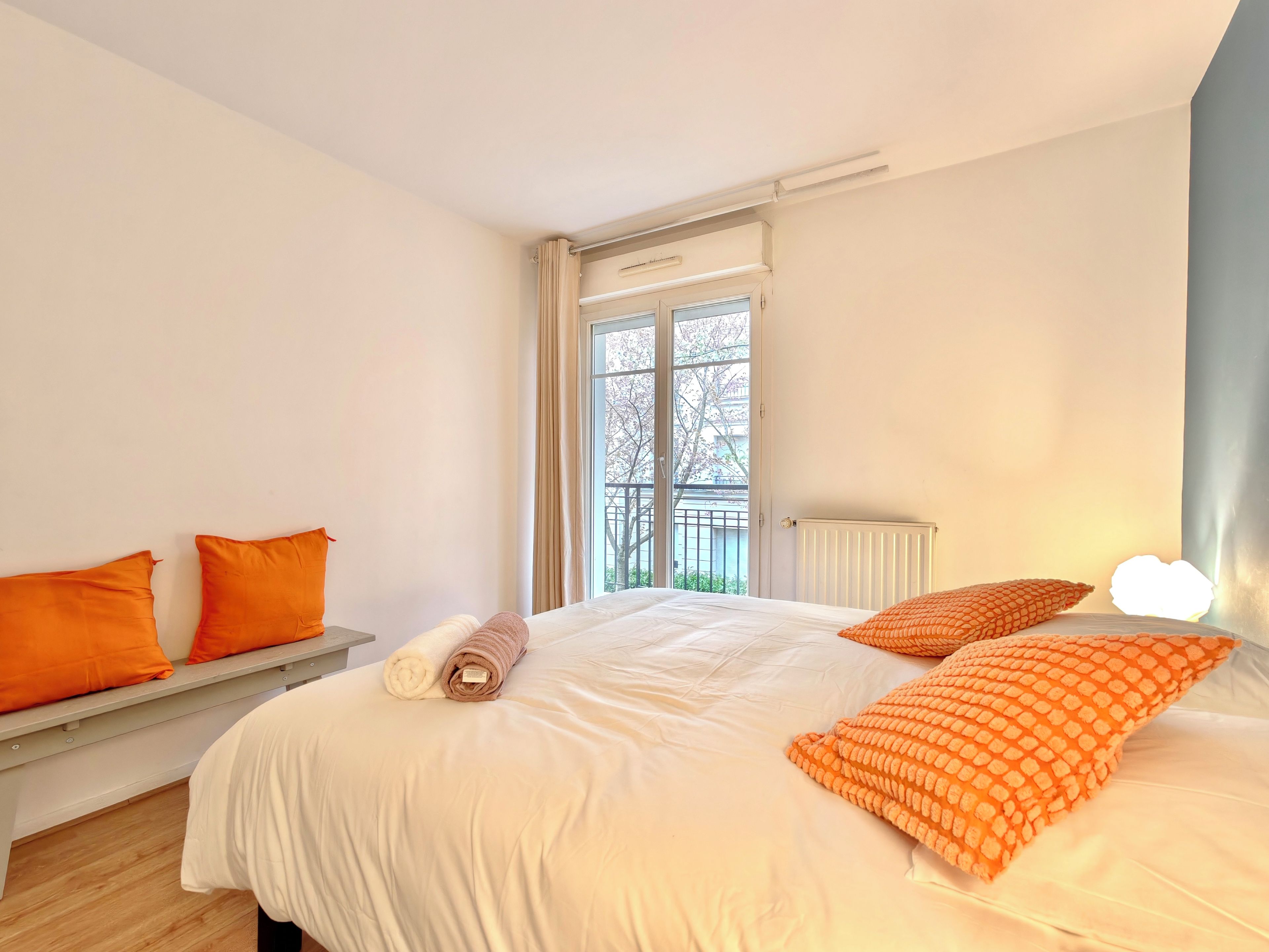 Quarto com cama, duas almofadas, um banco e janela.