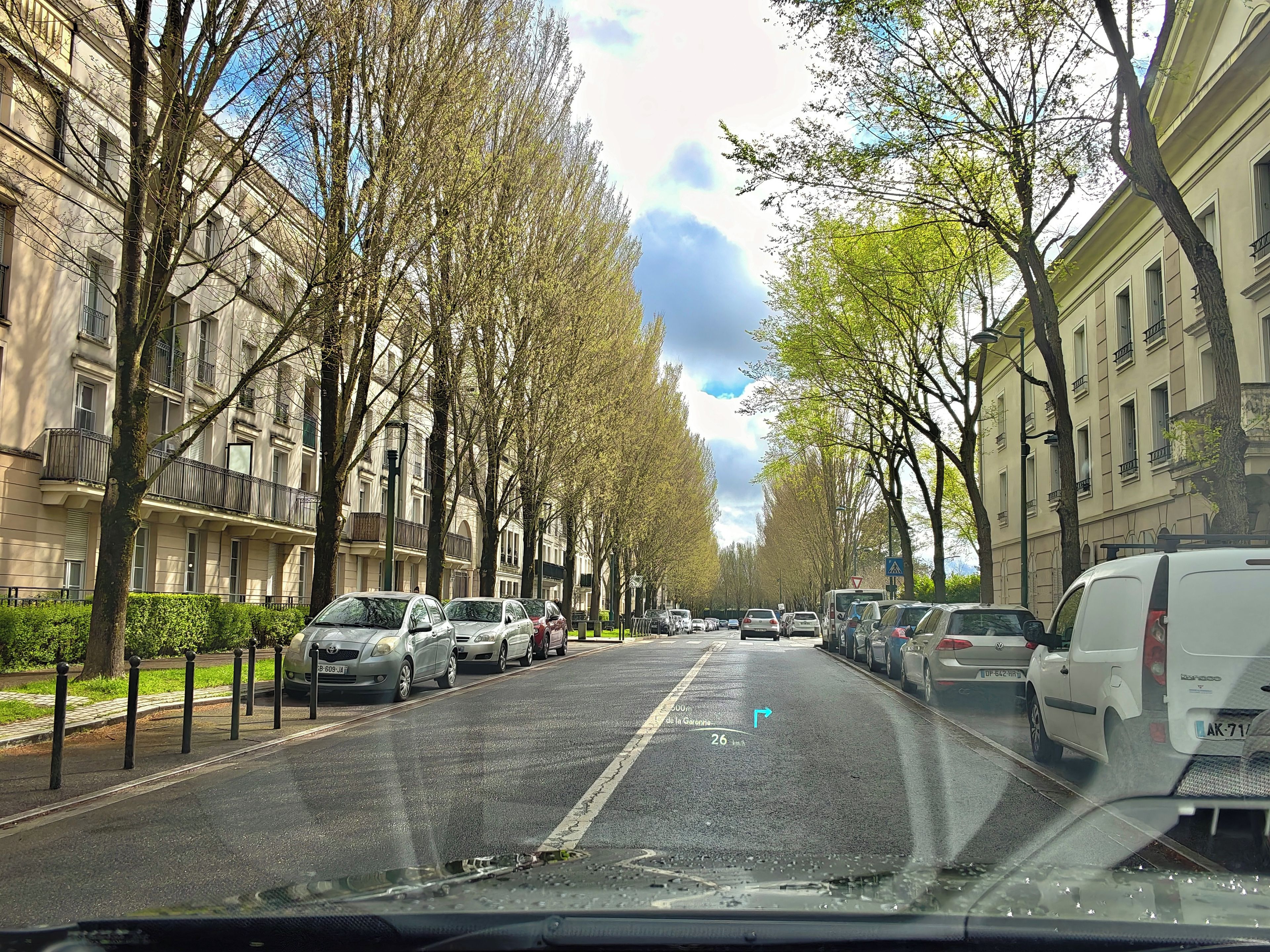 Een straat met geparkeerde auto's en bomen, met gebouwen aan beide zijden.
