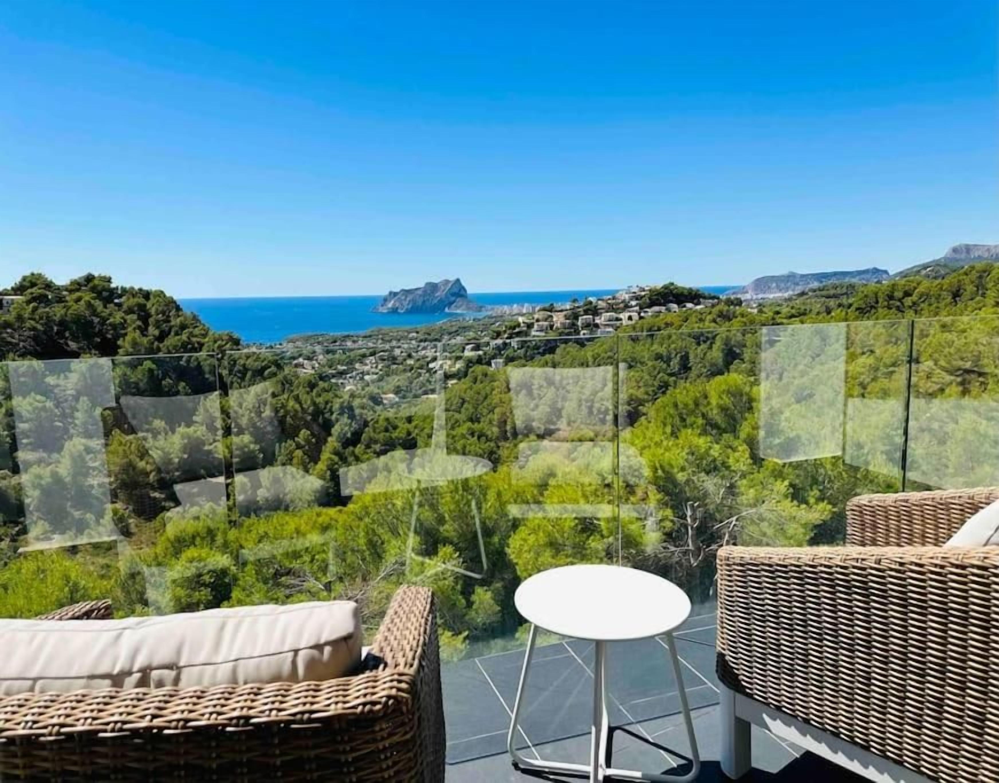 A balcony with wicker furniture and a view of the sea and hills.