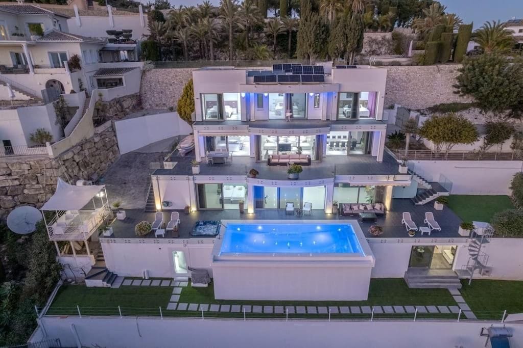 Een modern huis met meerdere verdiepingen, een zwembad, buitenmeubilair en zonnepanelen.
