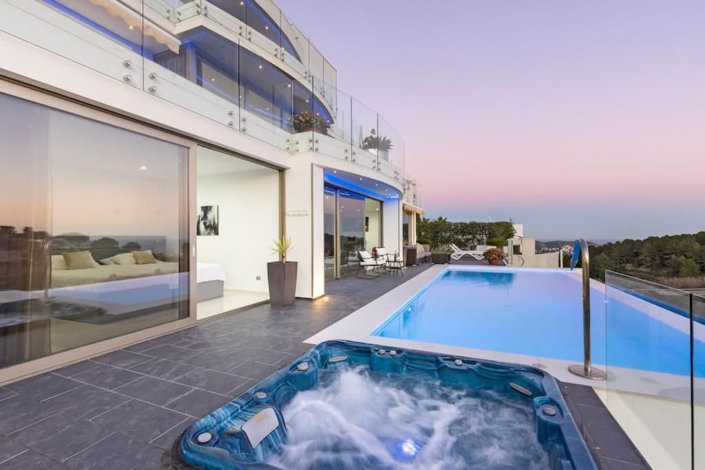 Un área de piscina moderna al aire libre con un jacuzzi, un espacio habitable con paredes de vidrio y vistas al paisaje circundante.