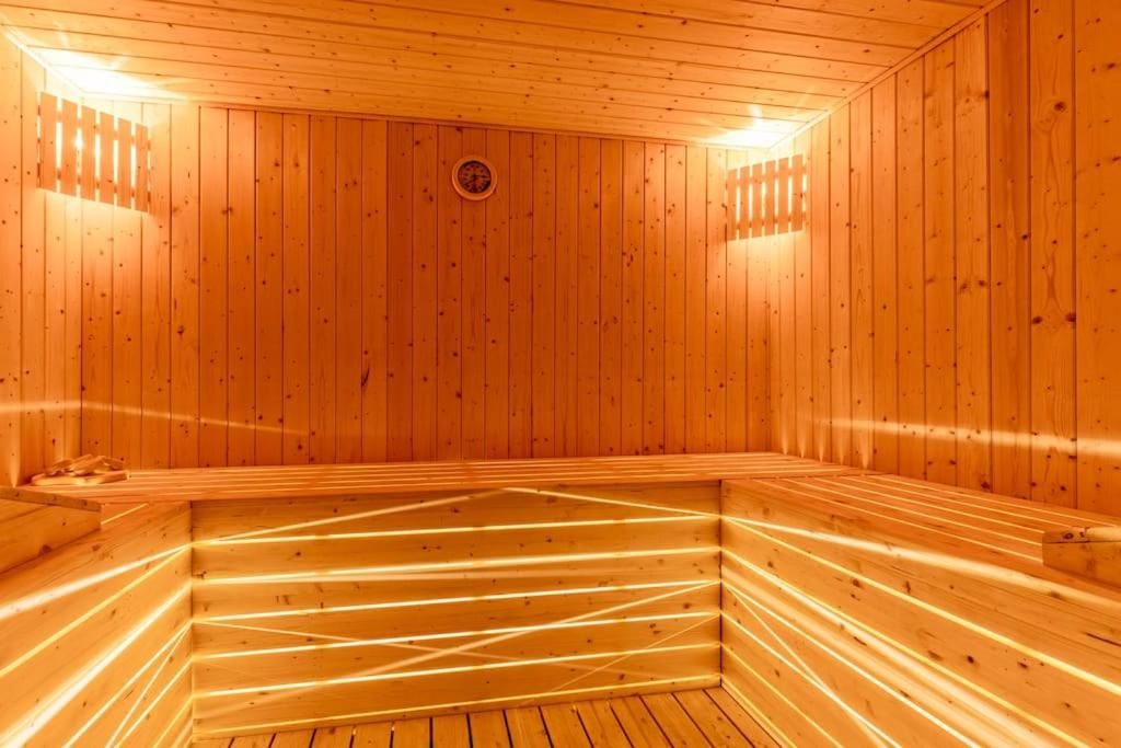 A sauna with wooden walls and benches, a visible ceiling vent, and a small circular vent on the wall.