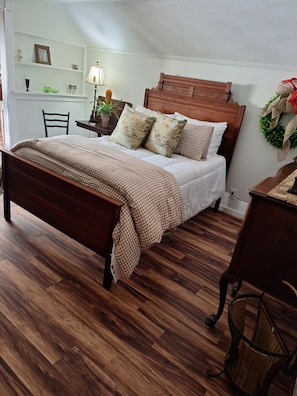 Quarto com cama de madeira, mesa de cabeceira com luminária e prateleira na parede com objetos decorativos.