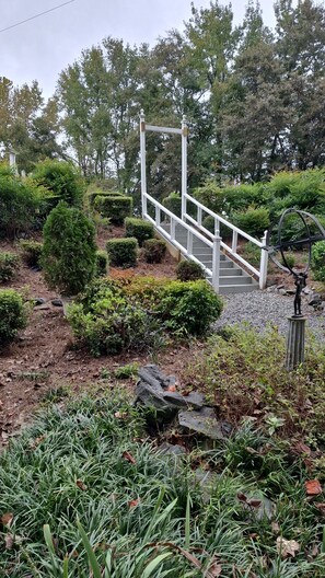 Een witte metalen trap die leidt naar een witte balustrade, omgeven door goed onderhouden struiken en bomen.
