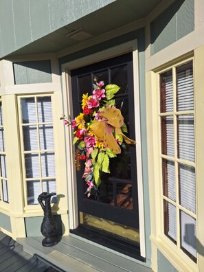 Uma porta de entrada com um arranjo floral, um vaso preto e uma janela com persianas.