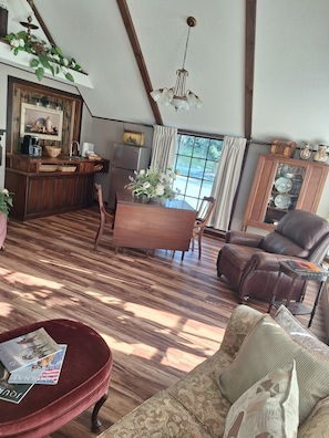 Uma sala de estar aconchegante com uma mesa de jantar de madeira, um sofá de couro e um banquinho vermelho com revistas.